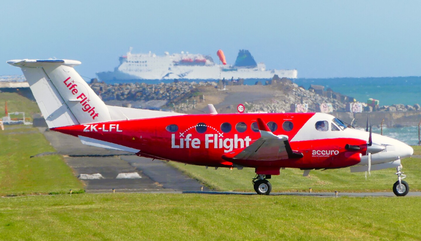Lifeflight plane on the runway at Wellington Airport with Interislander ferry in the background leaving Wellington Harbour