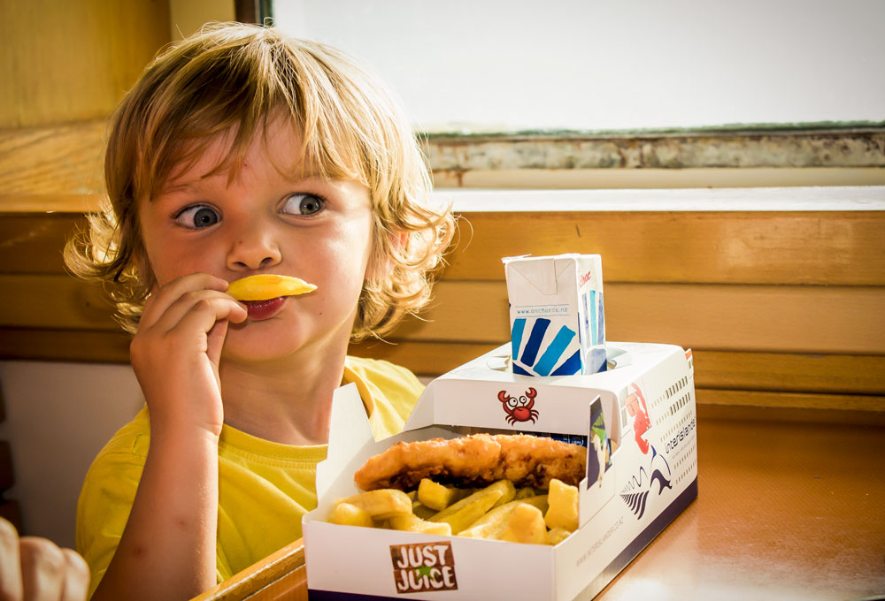 Child enjoying fish n chips served in a ferry-shaped box